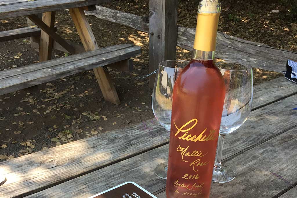 Bottle of Picchetti Mattie Rosé with two wine glasses on a wooden picnic table at Picchetti Winery, Cupertino