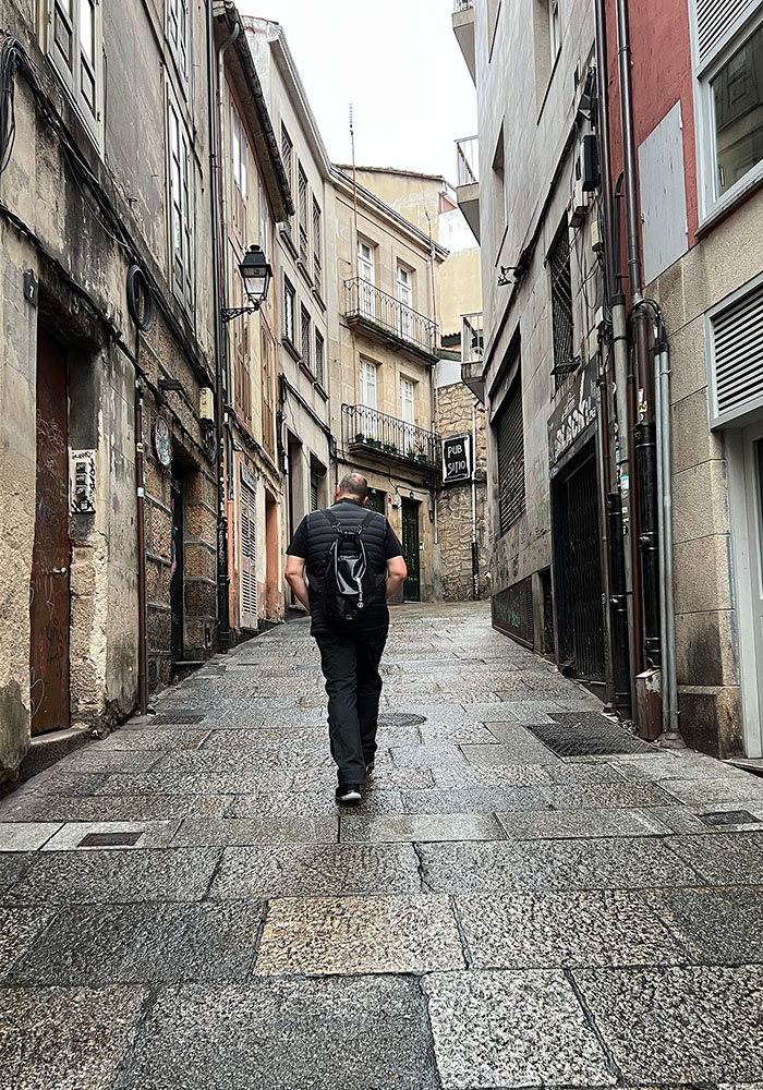 Man with backpack wandering through old town pedestrian free street, with high buildings on each side.